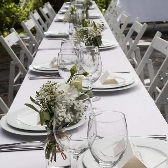 Lange gedeckte Hochzeitstafel mit weißen Holzstühlen und weißen Blumen